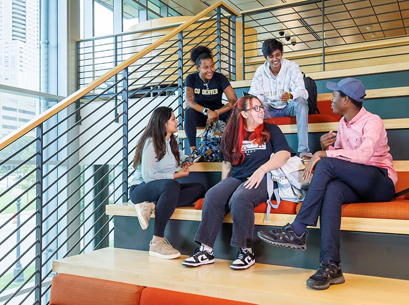 Group of students sitting on a well-lit staircase interacting with one another and talking. .