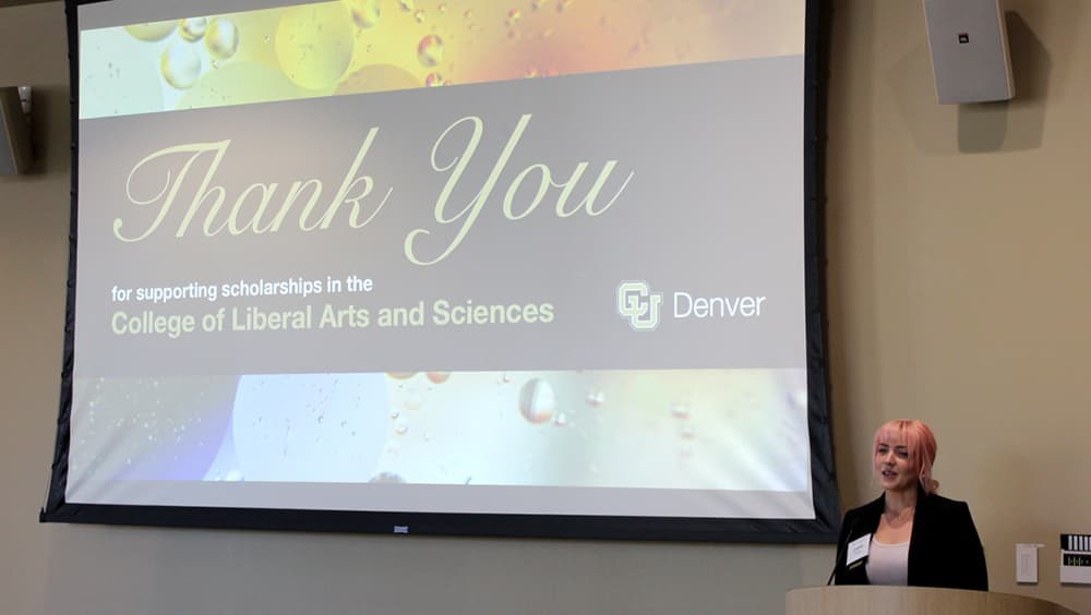 Student Elizabeth Kuhn standing at the lectern speaking in front of a big screen that reads 