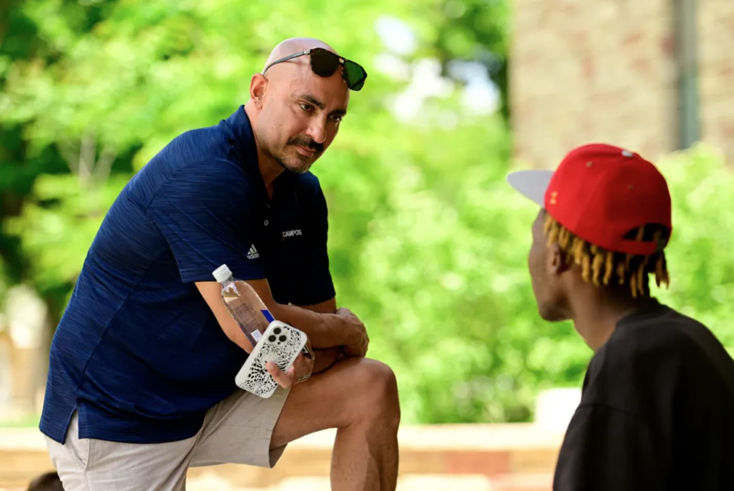 Marco Campos in a blue polo talking with a young person in an outdoor setting.