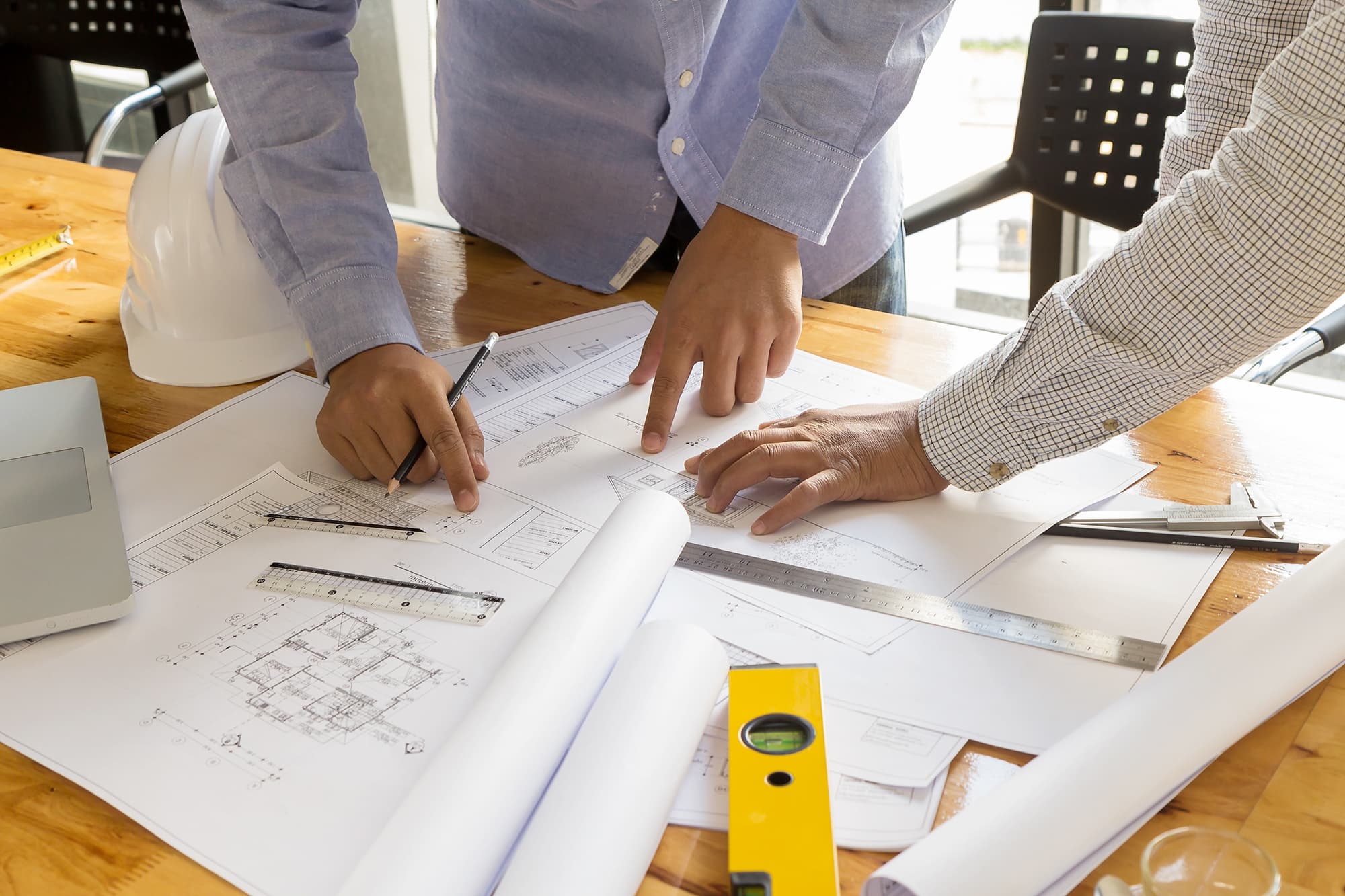 Overhead view of a table covered in architecture supplies and schematics with two sets of hands pointing and interacting.