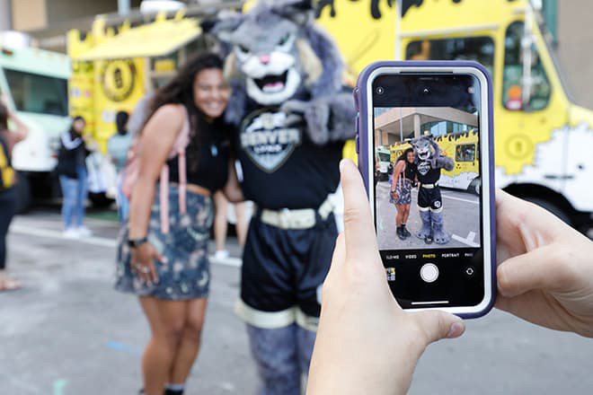 Two people posing for a photo being taken by a cell phone.