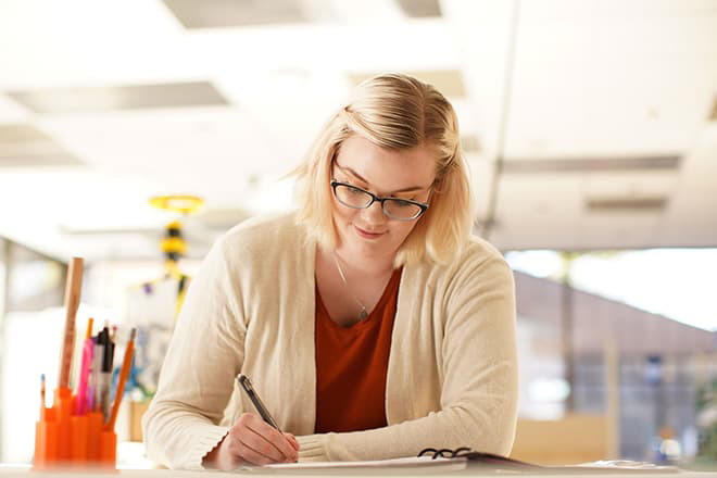 Blonde woman writing something with a pen and paper.