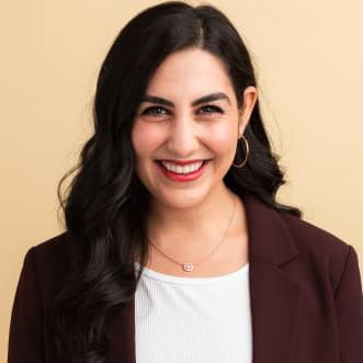 Ariana Lily Nikmanesh in a dark suit jacket and long, dark hair, smiling with her teeth.