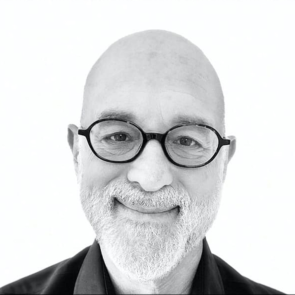 Headshot of Daniel Gilbert in a black collared shirt and dark, round-rimmed glasses, and a white beard and smiling without teeth.