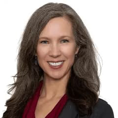 Darcy Kitching with long brown hair in a dark suit and smiling with her teeth.