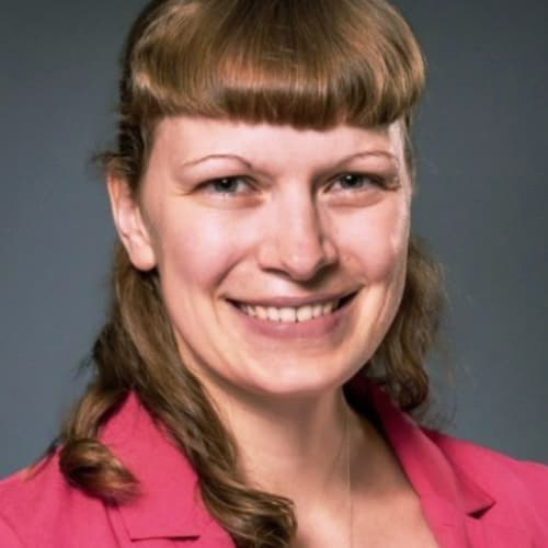 Kaitlin LaFlamme in a pink blazer, hair half pulled up with forward bangs, smiling with her teeth.