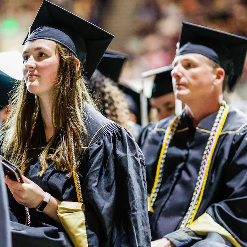 Students in commencement regalia sitting.