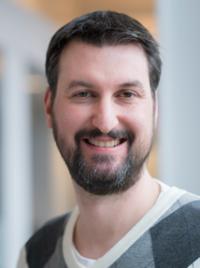 headshot of Alex Mihailidis from the shoulders up smiling in business casual sweater