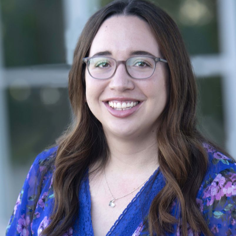 Headshot of Leslie Emery from the shoulders up smiling in floral business casual blouse