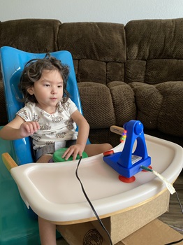 Young child sits contently in front of switch adapted fan toy.