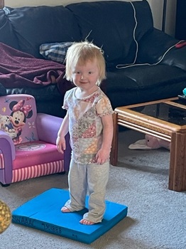 Young girl happily standing on a bright blue balancing pad.