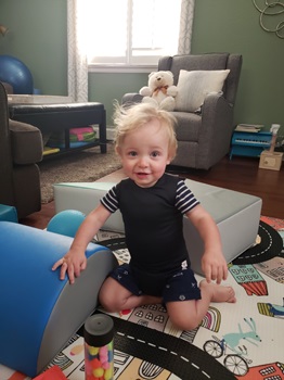 young boy smiling, sitting in the middle of his living room full of toys, wearing a SPIO vest