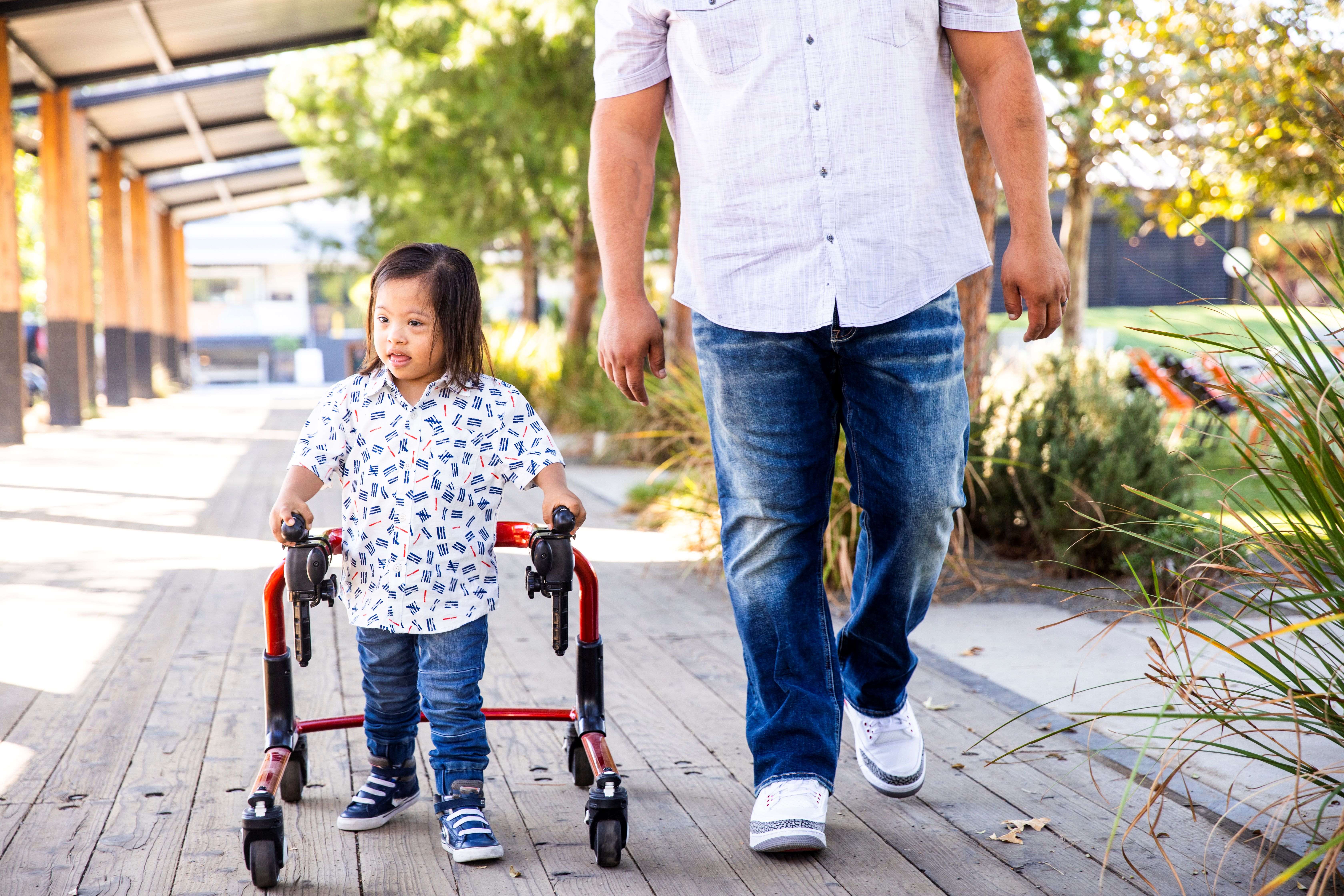 A child using a walker walks next to an adult