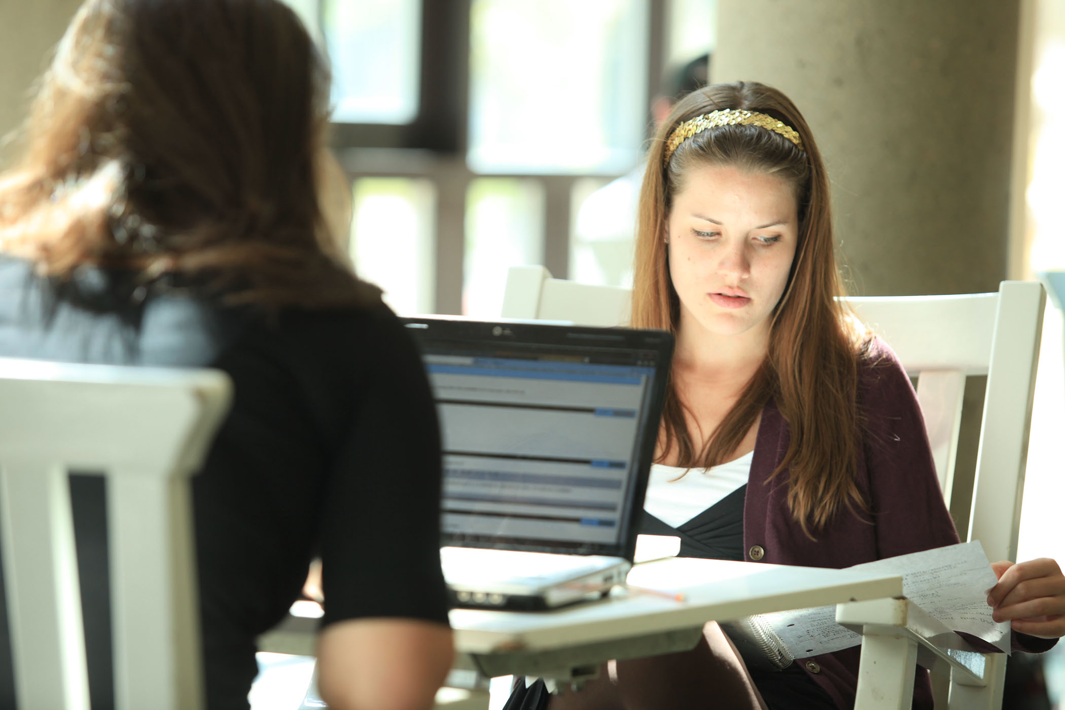 Two young women work together at a table with a laptop.